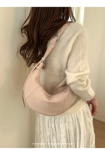 Close-up of a minimalist light pink crescent shoulder bag paired with a cream sweater