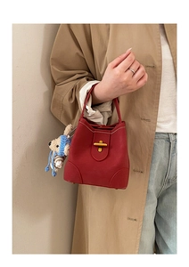 Close-up of wine red bucket bag with gold clasp and a cute bear charm accessory
