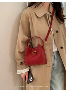 Detailed view of red leather bucket bag with gold T-buckle worn with a khaki trench coat
