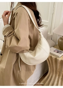 Detailed view of cream crescent hobo bag with pebble leather texture worn with a trench coat