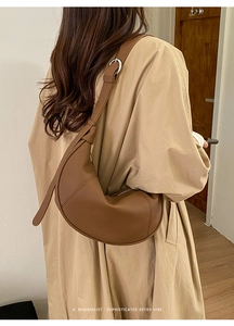 Brown leather crescent crossbody bag styled with a long trench coat for a retro vibe