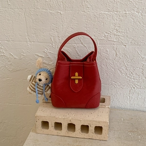 Gros plan d'un sac seau en cuir rouge avec fermoir doré en croix et breloque lapin