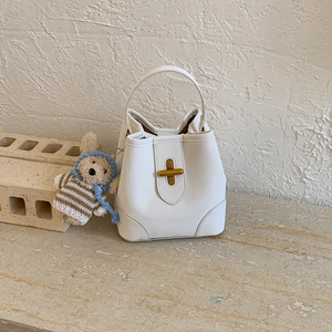 Détail du sac seau crème minimaliste avec fermoir doré et charmant ours en peluche attaché