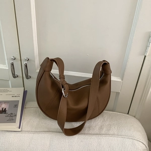 Detail of a brown lychee pattern leather crescent bag with silver zipper and wide strap