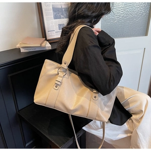 Close-up of beige leather tote bag featuring refined stitching and metal ring details