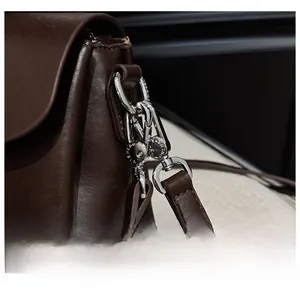 Detail of silver metal hook and refined leather texture on a dark brown shoulder bag