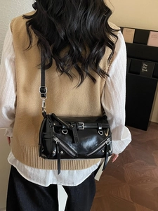 Minimalist black PU leather crossbody bag with metal zippers and buckles in an indoor setting