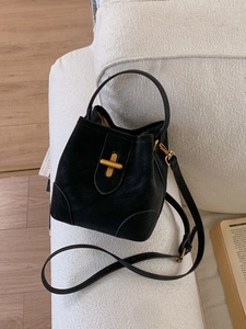 Sac seau minimaliste en cuir noir mat avec fermoir doré posé sur un canapé blanc
