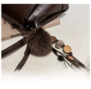 Close-up of brown faux fur pompom and wooden beads bag charm on a square crossbody bag