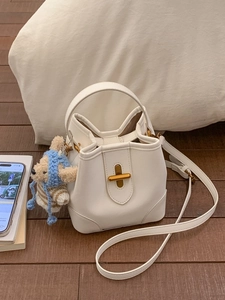 Sac seau blanc crème avec fermoir doré et breloque ours en peluche sur un coussin moelleux