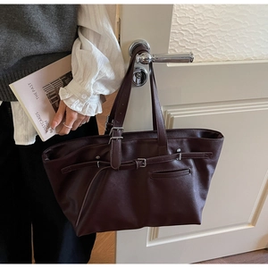 Détail du grand sac cabas en cuir marron foncé avec boucle rétro accroché à une porte blanche