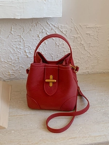 Sac seau minimaliste en cuir rouge avec boucle dorée en croix sur fond de pierre blanche