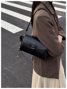 Close-up of black matte shoulder bag with fringe tassel and fur ball charm on urban street