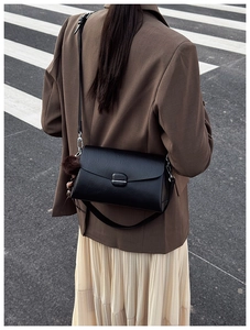 Detail of a matte black leather shoulder bag with a plush charm and adjustable strap