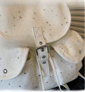 Détail des motifs d'étoiles argentées et des boucles métalliques du sac à dos beige