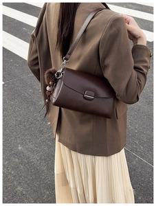 Detail of dark brown faux leather shoulder bag with plush ball and tassel on a wide strap