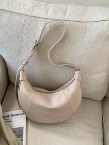 Minimalist beige half-moon shoulder bag with pebble leather texture and adjustable strap