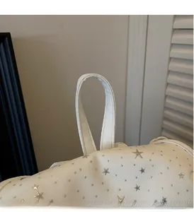 Détail de la poignée en toile et des rivets étoiles argentés sur le sac à dos blanc