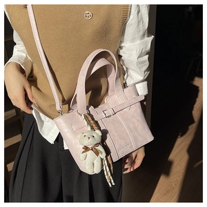 Detail of lavender leather bucket bag with top handles and a white plush bear charm
