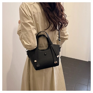 Sac seau noir texture cuir porté par un mannequin en trench-coat beige élégant