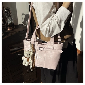 Detail of pink faux leather bucket bag featuring decorative buckle and plush bear charm