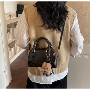 Detail of dark brown glossy shell bag with plush dog charm and detachable strap