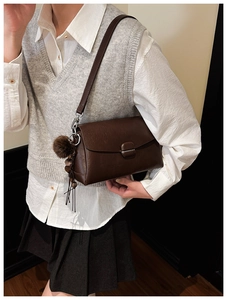 Close-up of a brown leather crossbody bag featuring a metal buckle and plush charm detail