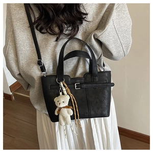 Detail of black leather bucket bag featuring metal buckle and cute teddy bear charm