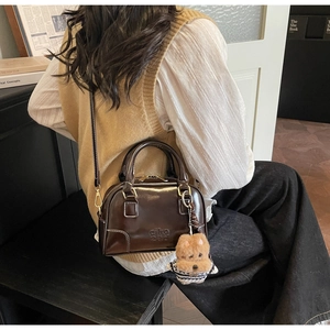 Detail of dark brown patent leather shell bag with gold hardware and puppy charm