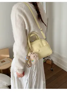 Detail of light yellow crossbody bucket bag featuring a cute plush bear charm on strap