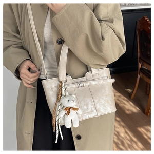 Detail of light beige bucket bag with teddy bear charm and belt buckle decoration