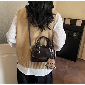 Detail of dark brown leather Boston bag with teddy bear charm and adjustable strap
