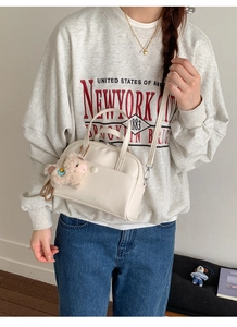 Detail of a beige Boston bag with piglet plush keychain and adjustable strap