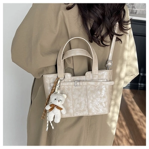 Detail of cream bucket bag with textured leather, plush bear charm, and shoulder strap