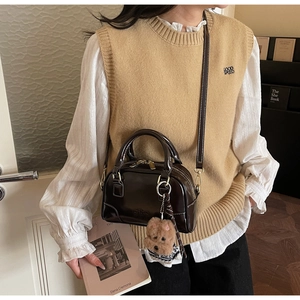 Detailed view of a dark brown glossy shell bag with golden metal and plush charm