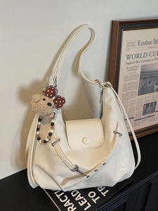 Minimalistische beige Halbmond-Tasche mit Bärenanhänger und Perlenkette auf schwarzem Tisch