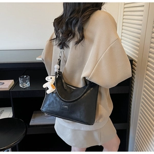 Détail du sac hobo noir avec breloque poney blanc et étiquette sur pull beige