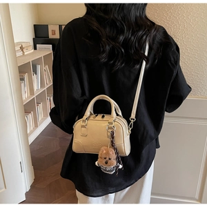 Beige Boston bag with teddy bear charm shown from back view on a female model