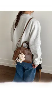 Detail of a brown vintage Boston bag with plush bear charm and adjustable strap