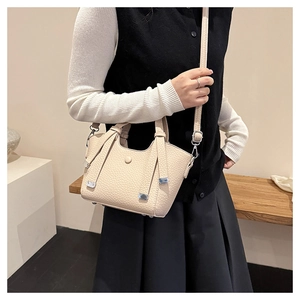 Détail du sac seau blanc cassé avec motif litchi, fermoir argenté et bandoulière