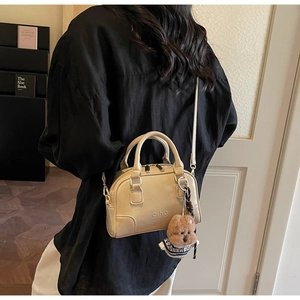 Detail of beige shell Boston bag featuring Gino Bag logo and cute bear accessory