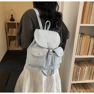 Detail of light blue star-patterned canvas backpack worn by a model in a library