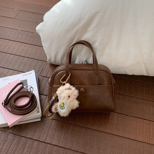 Detailed view of brown Boston bag with alpaca plush charm on a wooden background
