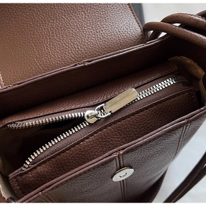 Details einer dunkelbraunen Ledertasche mit silbernem Magnetverschluss und Reißverschluss
