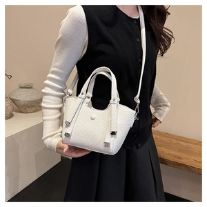Détail du sac seau blanc en cuir grainé avec finitions argentées sur un banc en bois