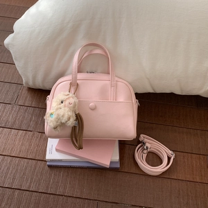 Pink mini Boston bag with plush alpaca charm on wooden floor with natural lighting