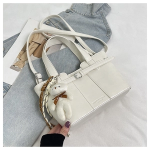 Detail of white leather bucket bag with plush bear charm and striped silk scarf