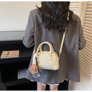 Detail of a creamy white mini shell bag with a cute plush bear charm and sleek leather