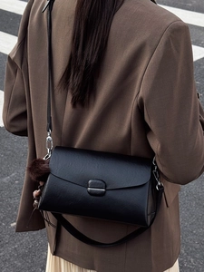 Classic black leather crossbody bag with silver buckle and plush ball charm on model