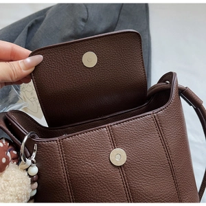 Detail der braunen Leder-Tasche mit Litschimuster, Magnetverschluss und Anhängern